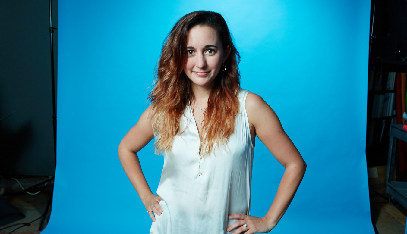 Photograph Portrait of Sara Cannon smiling in front of bright blue background with hands on hips